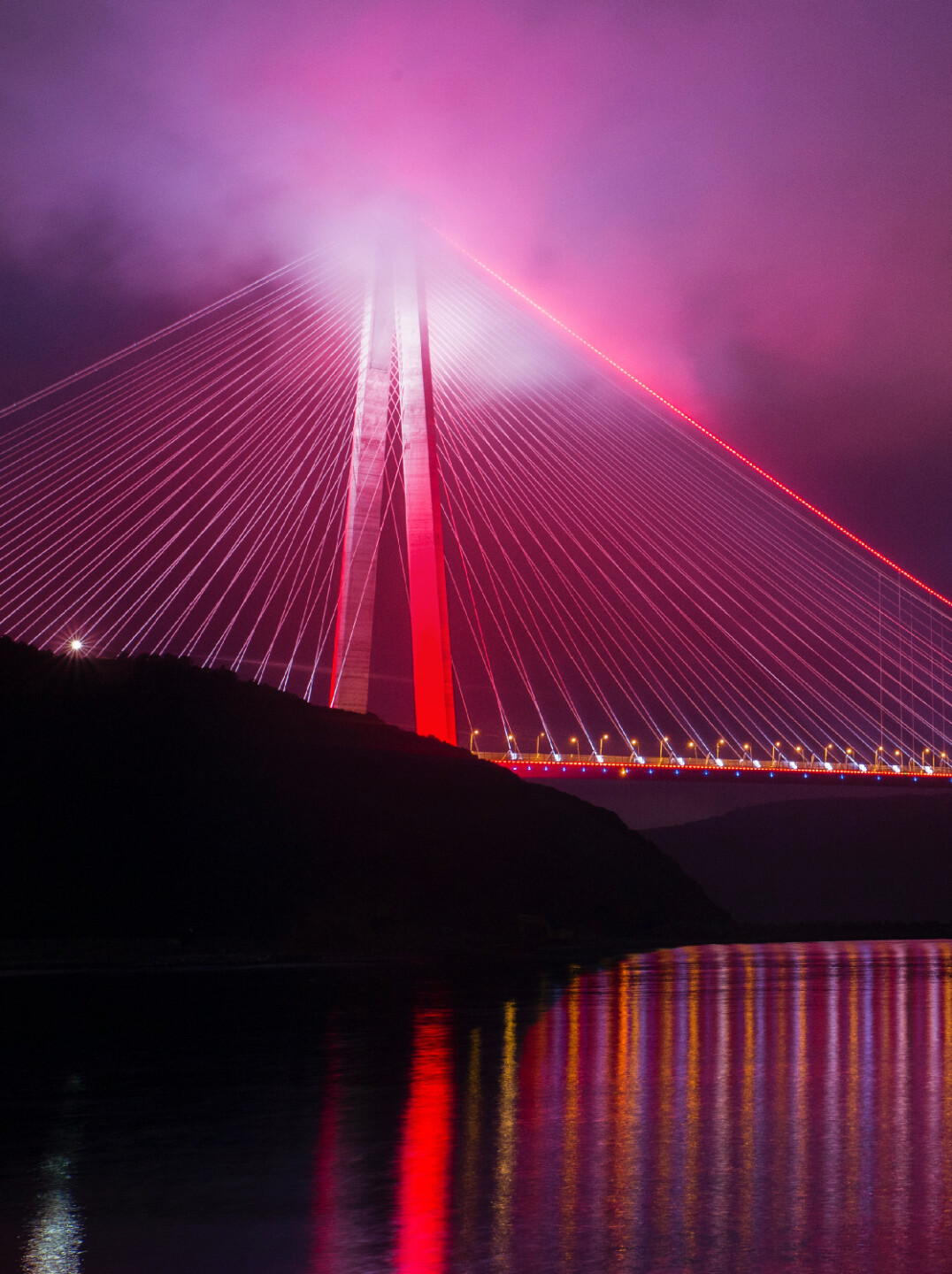 Golden gate bridge with a pink hue, lit up on a cloudy night