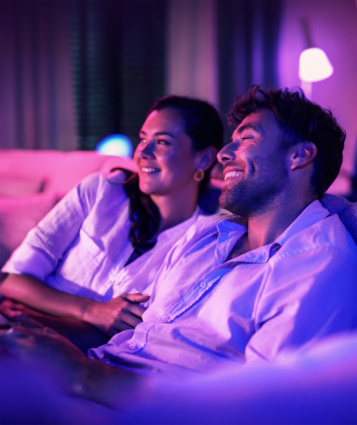 A couple sitting on the sofa watching the TV is a purple-lit room